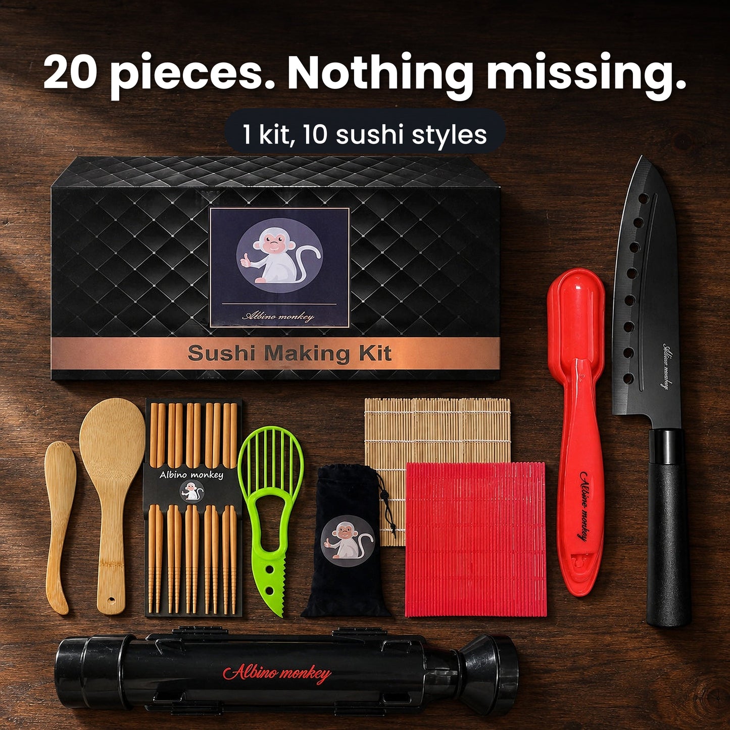 All 20 pieces of the Albino Monkey sushi making kit arranged on a dark walnut table: gift box, bazooka roller, sashimi knife, two rolling mats, nigiri mold, avocado slicer, rice paddle, spreader, chopsticks and storage bag